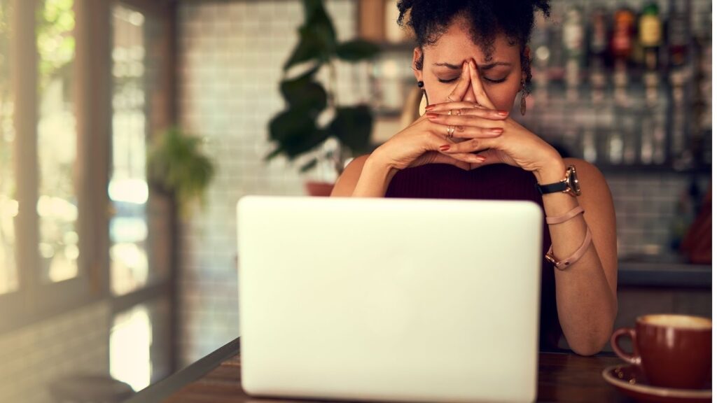ノートパソコンを前に頭を抱え、ストレスを感じている様子の女性。
